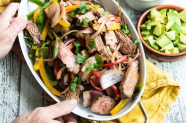 Steak fajitas in a white serving dish.