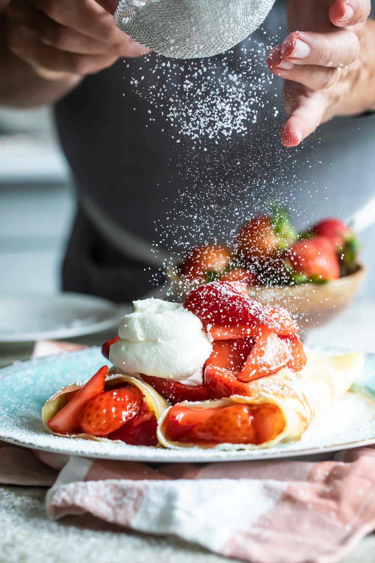 Strawberry crepes being dusted with powdered sugar.