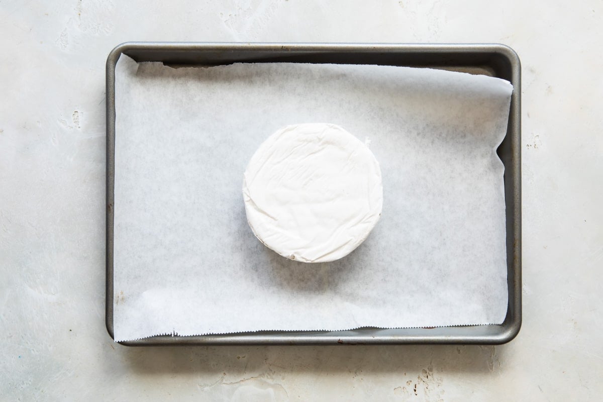 Brie cheese on a parchment paper lined baking sheet.