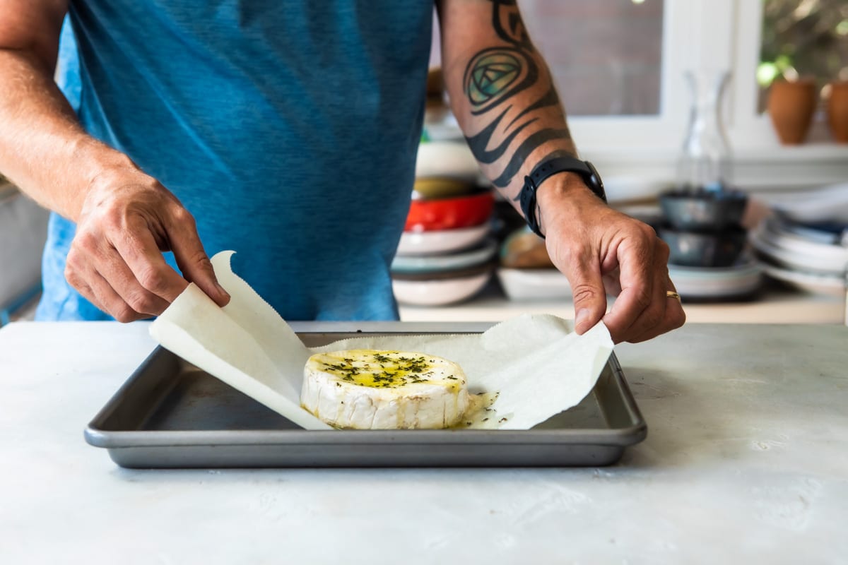 Someone lifting brie cheese off of a baking sheet.