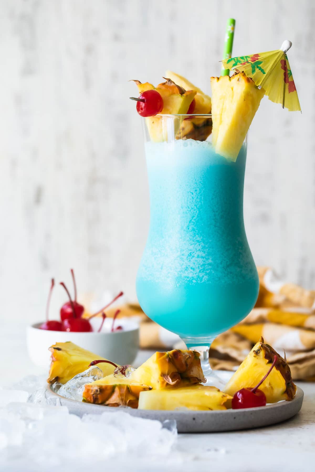 A Blue Hawaiian cocktail surrounded by pineapple and maraschino cherries.