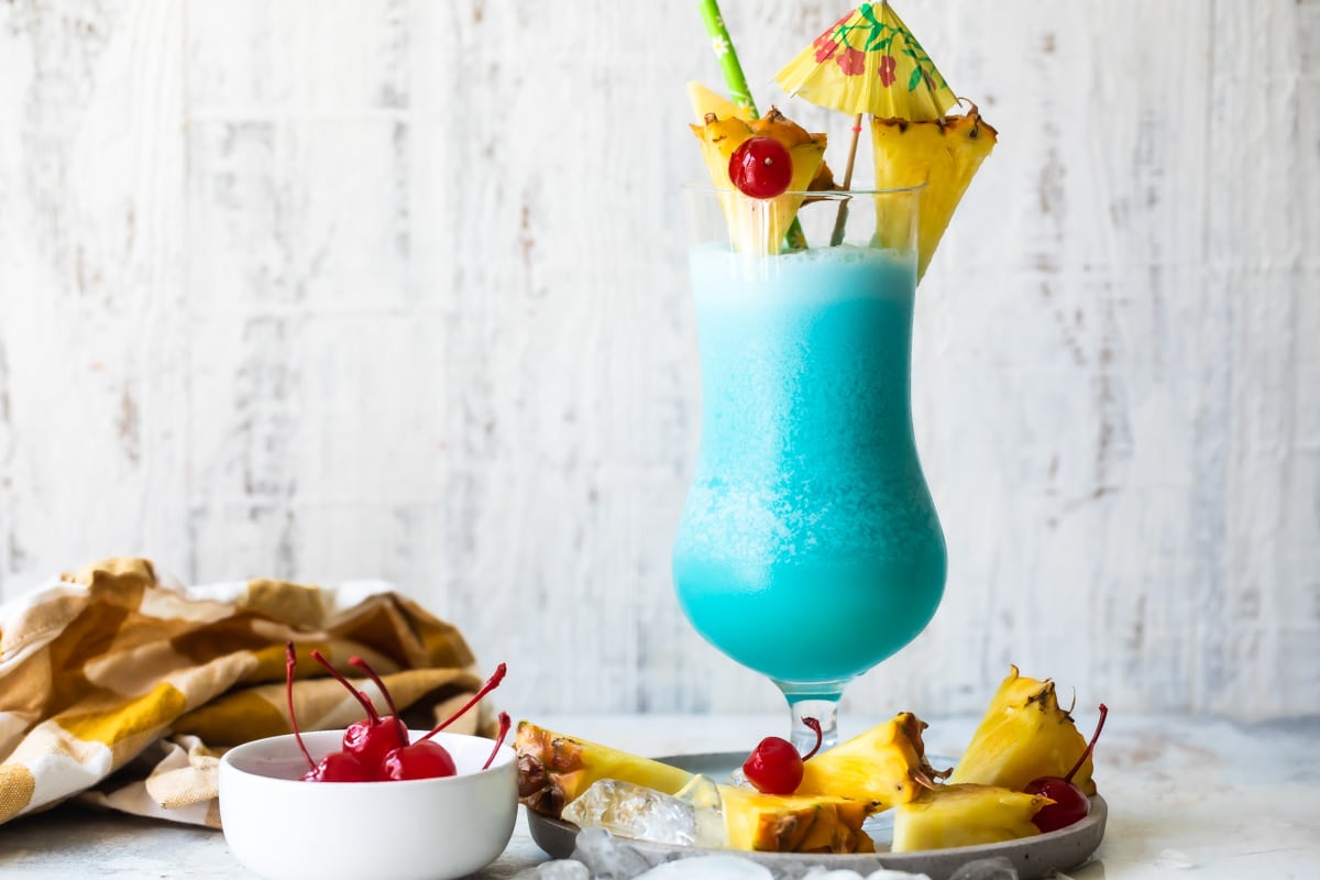 A Blue Hawaiian cocktail surrounded by pineapple and maraschino cherries.