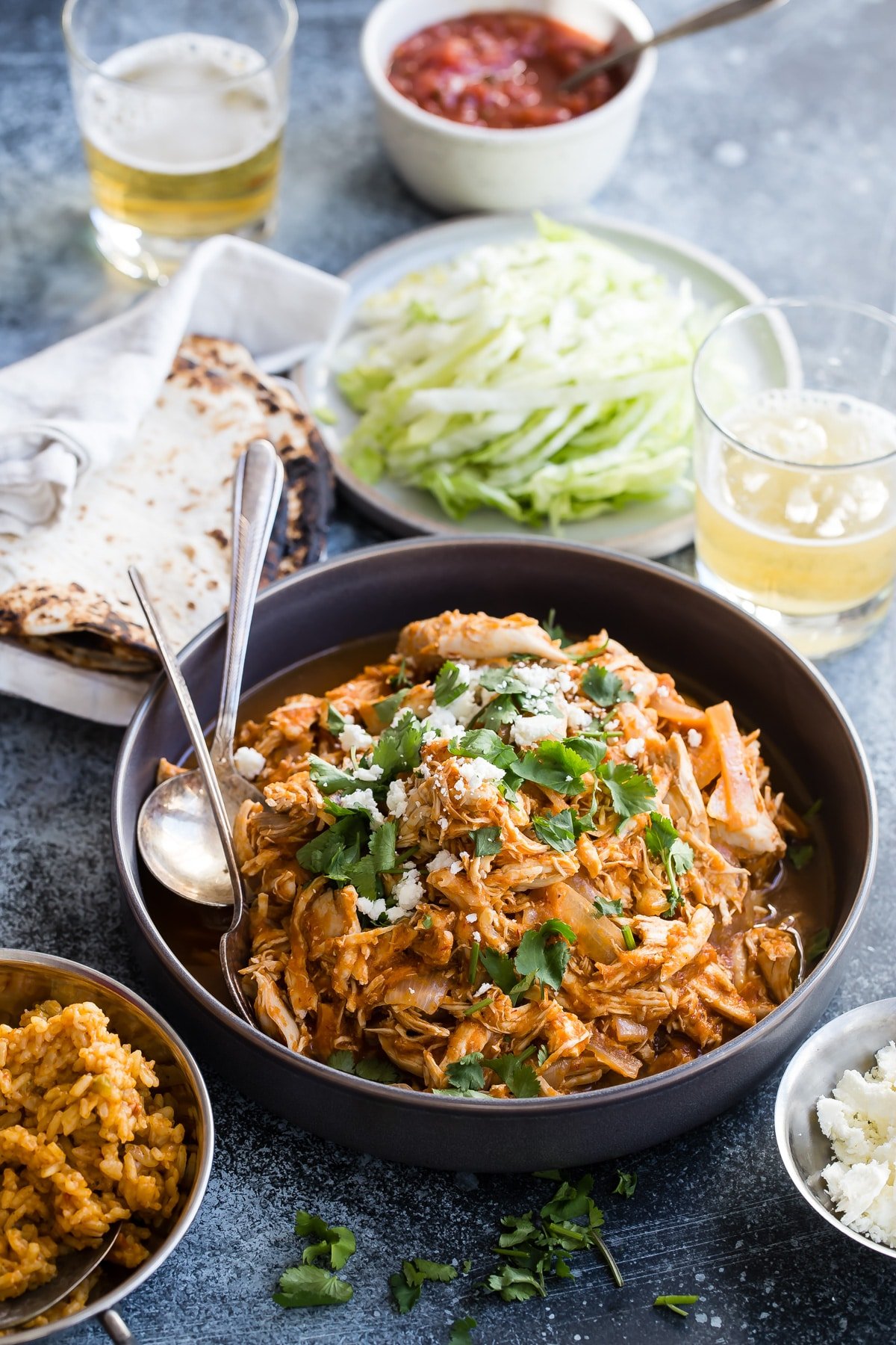 Chicken tinga in a bowl with tortilla shells and lettuce behind.