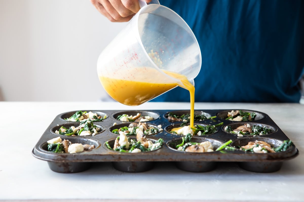 Someone pouring egg mixture into a muffin tin with egg muffin mixture.