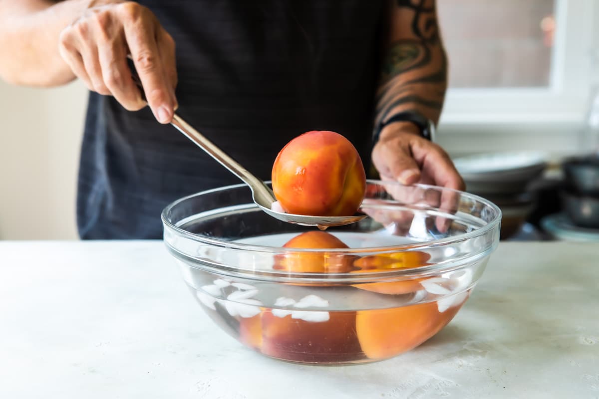 Someone pulling a whole peach out of an ice bath.