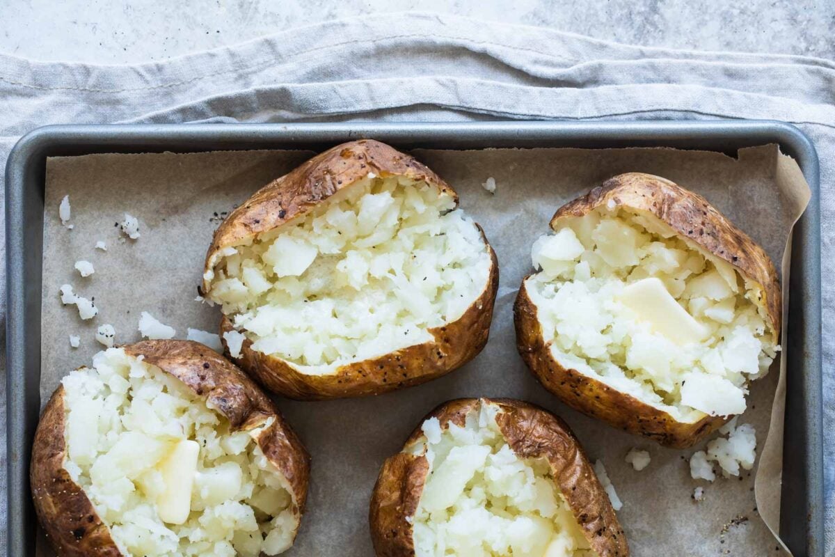 4 baked potatoes on a baking sheet.