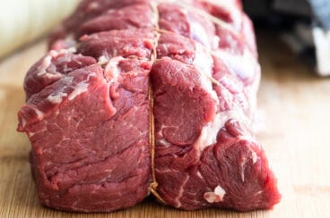 A beef tenderloin tied on a wooden cutting board.