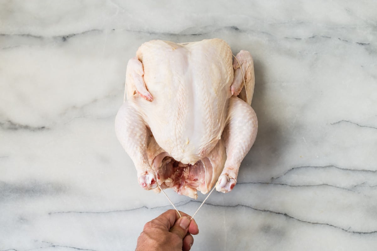 Someone trussing a raw chicken.