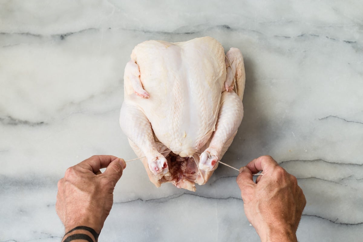 Someone trussing a raw chicken.