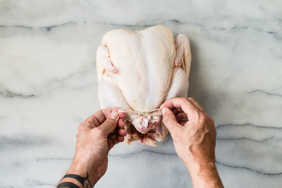 Someone trussing a raw chicken.
