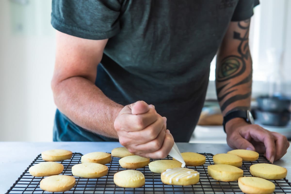 Lemon cookies being iced on a cooling rack.