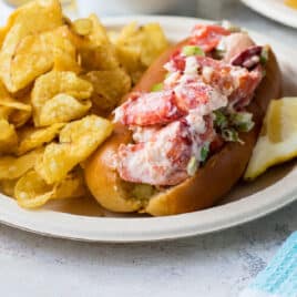 White plates with lobster rolls, potato chips, and lemon slices piled on top.
