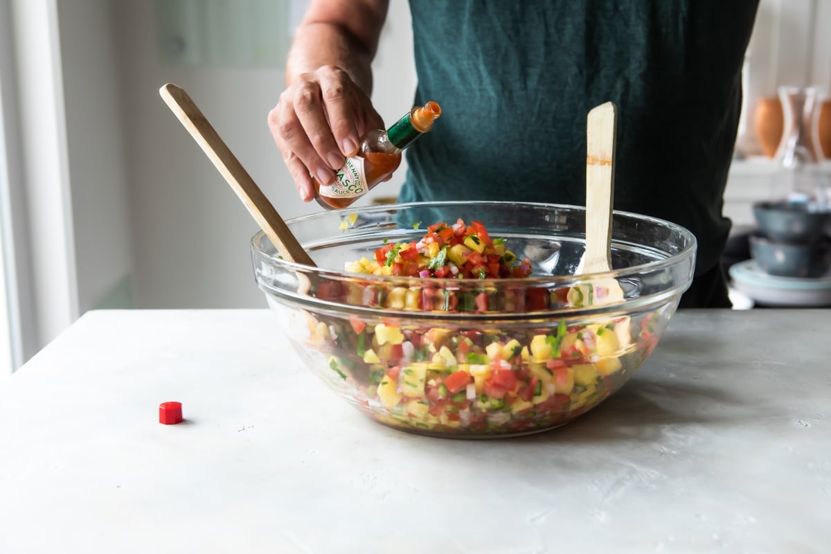 Someone adding tabasco sauce to pineapple salsa.