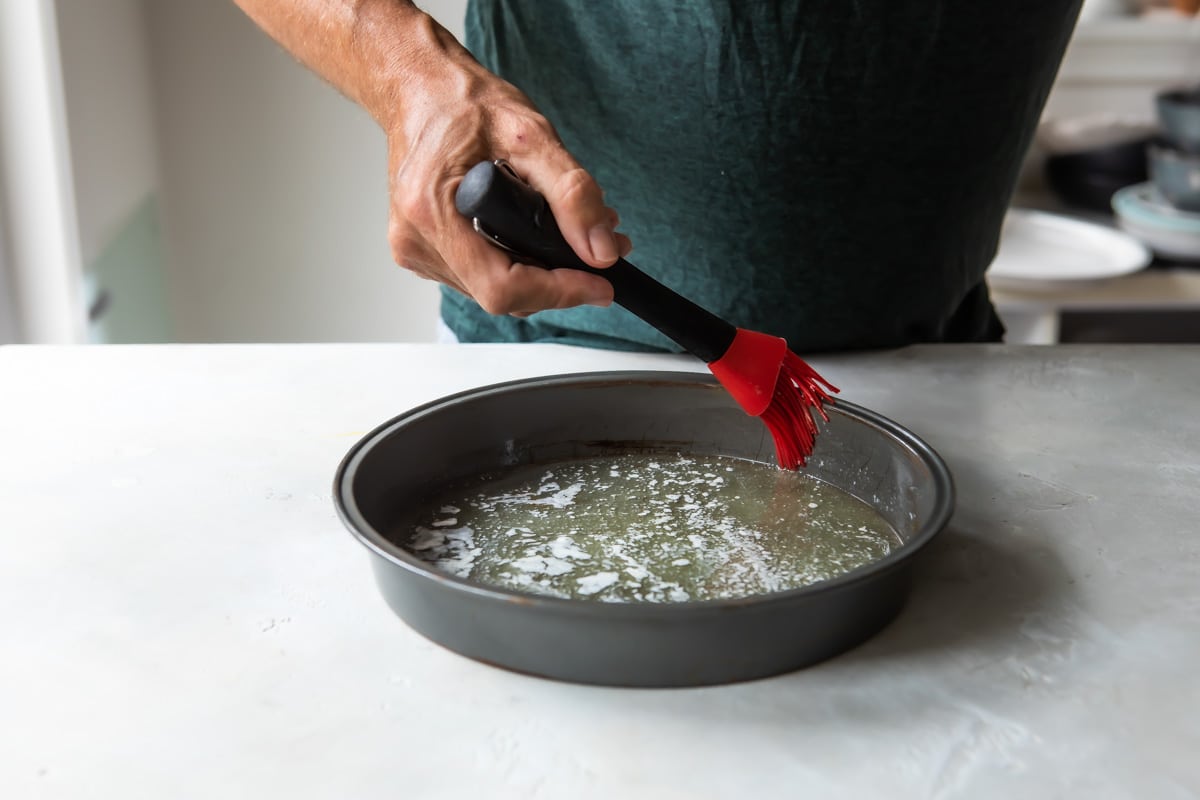 Melted butter being spread in a cake pan for pineapple upside down cake.