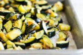 Roasted zucchini on a silver baking sheet.