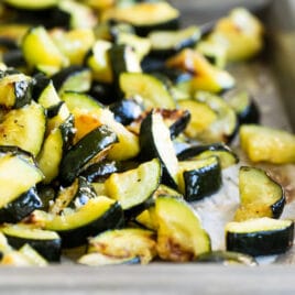 Roasted zucchini on a silver baking sheet.