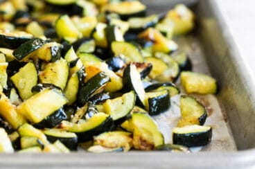 Roasted zucchini on a silver baking sheet.