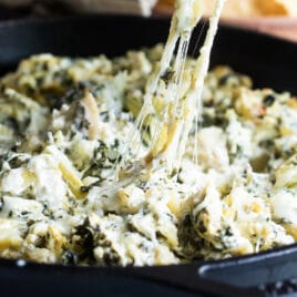Spinach artichoke dip being scooped out of a cast iron pan.