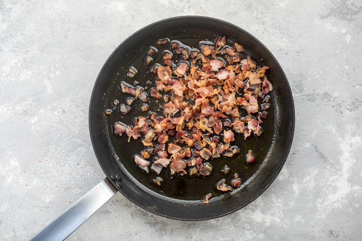 Sweet potato hash ingredients cooking in a black skillet.