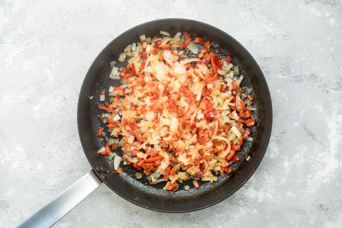 Sweet potato hash ingredients cooking in a black skillet.
