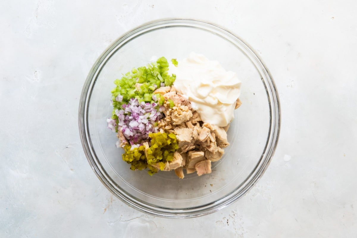 Ingredients for tuna salad in a clear bowl before being mixed.