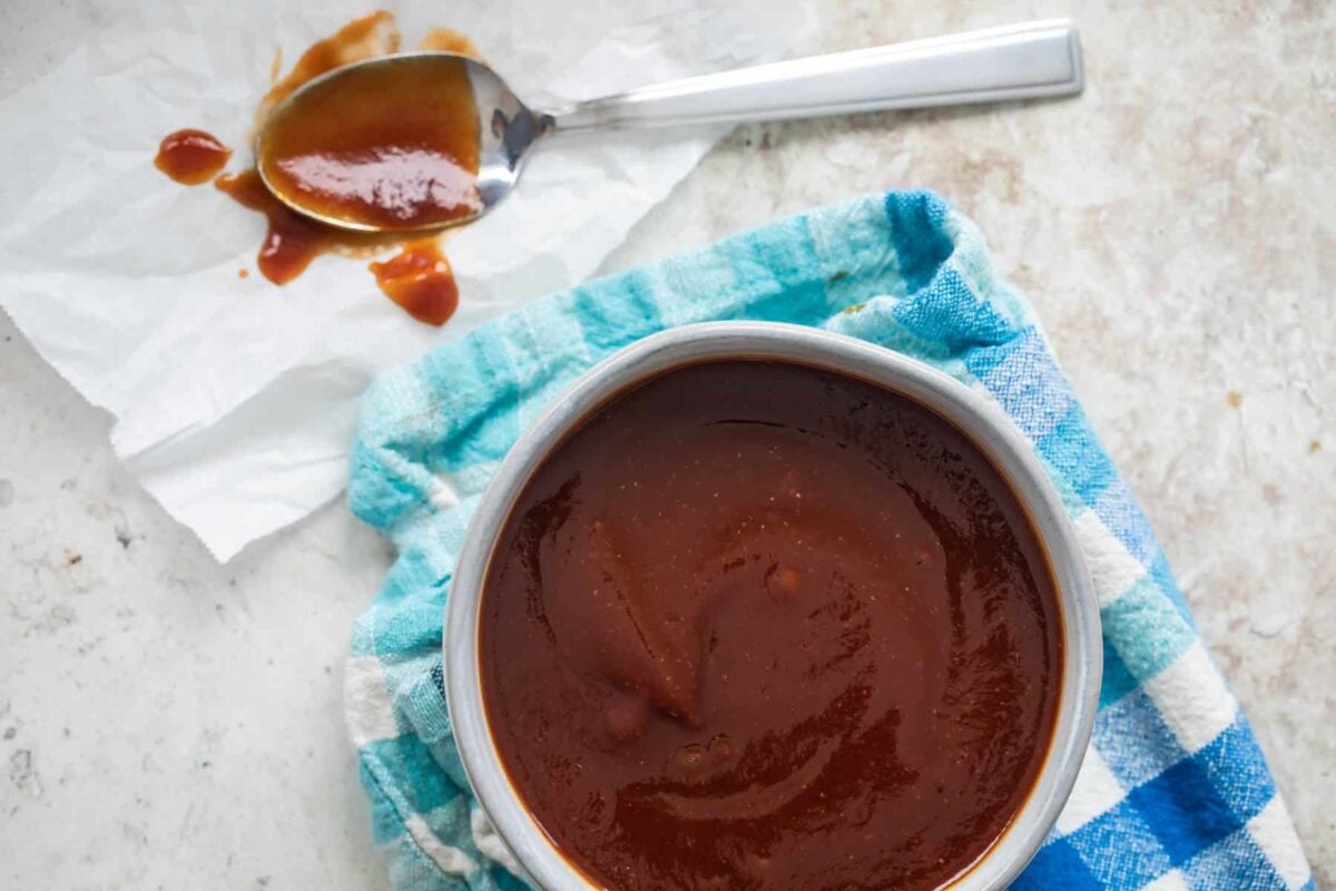 A bowl of barbecue sauce with a checkered towel under it.