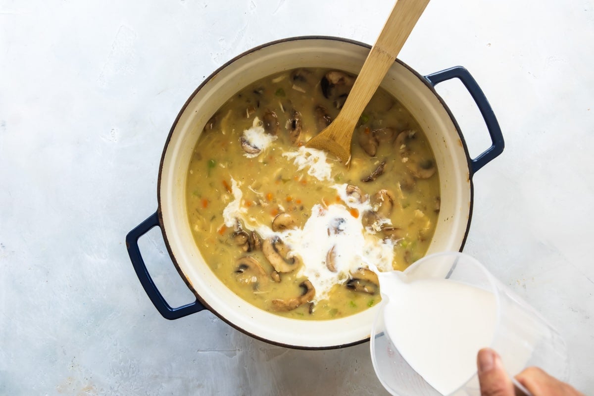 Someone pouring cream into chicken wild rice soup.