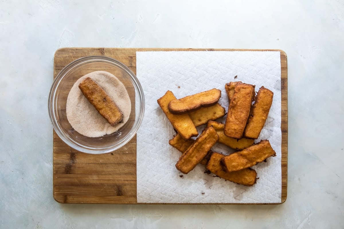 Rolling French toast sticks in a cinnamon-sugar topping.