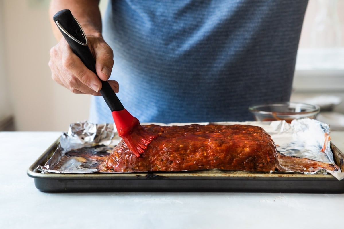 Someone brushing sauce on a meatloaf.