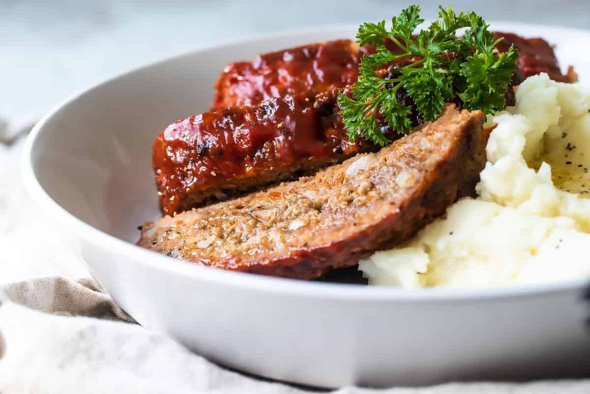 Three slices of meatloaf and mashed potatoes on a white plate.