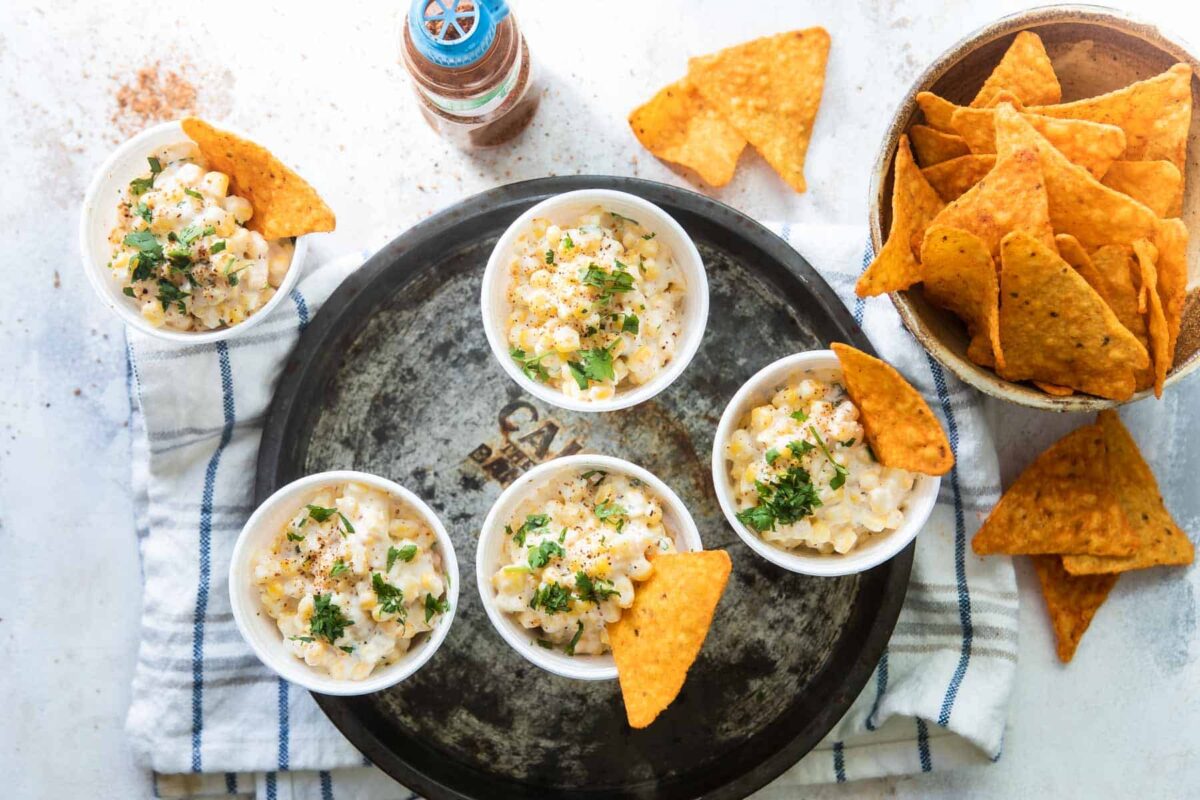 Mexican corn salad in five cups next to a bowl of Doritos.