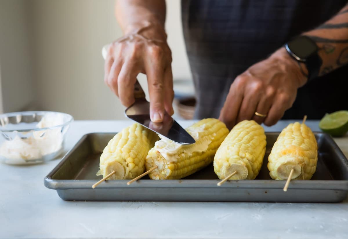 Corn on the cob on skewers, set on a baking sheet.