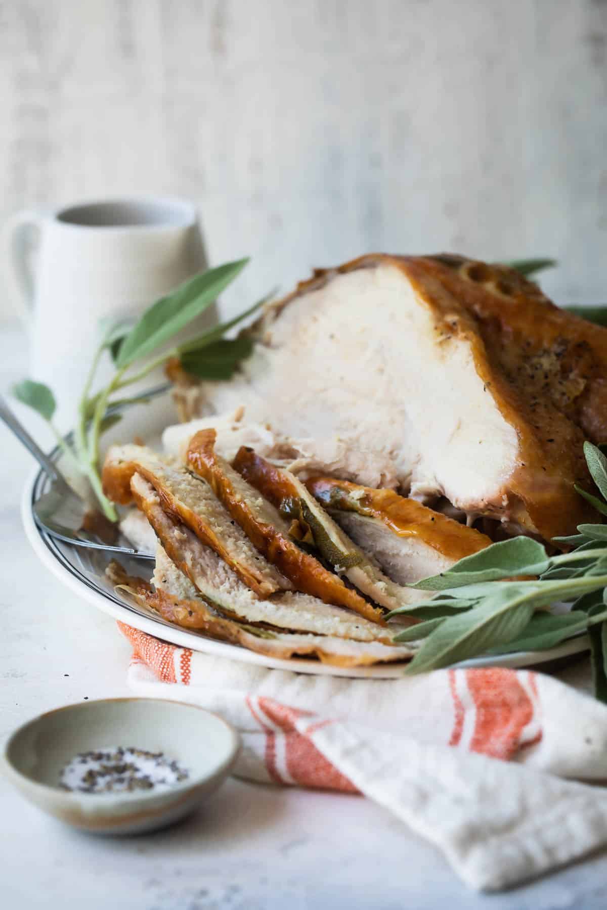 A platter of roasted turkey breast garnished with fresh sage.