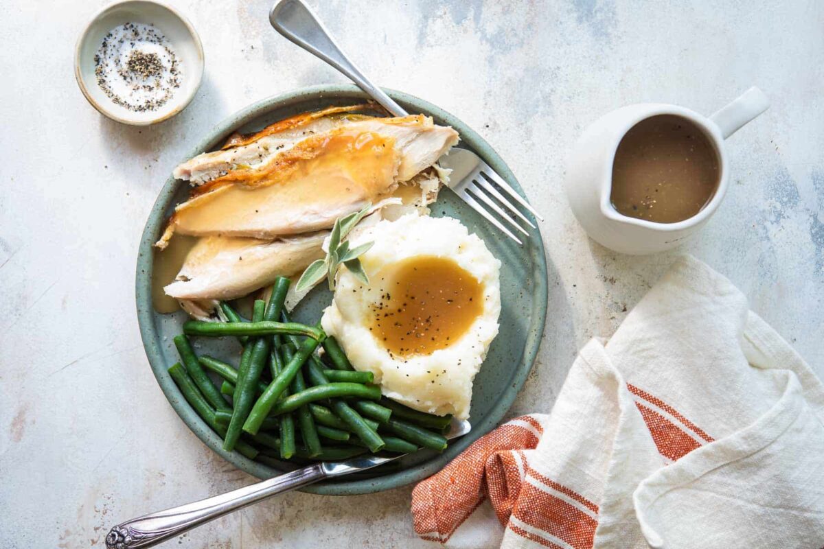 A plate of turkey breast with gravy, mashed potatoes, and green beans.