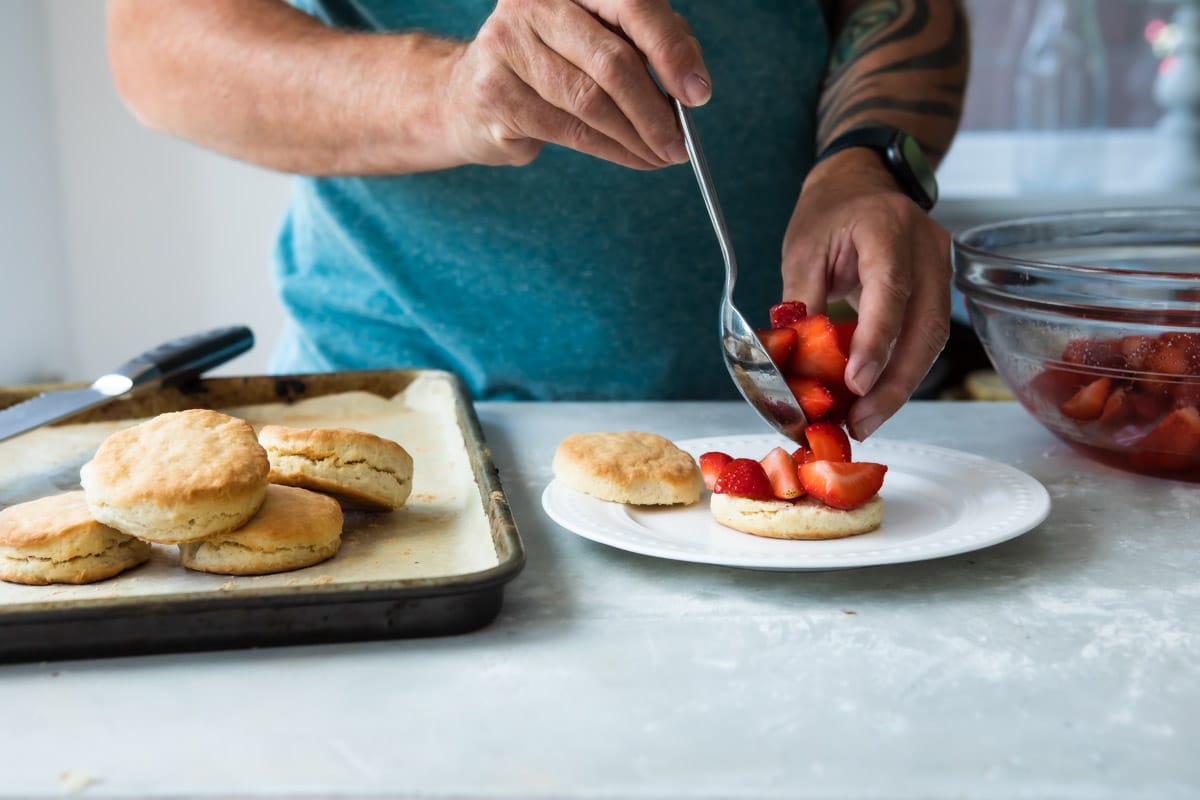 Someone spooning strawberries on a biscuit for strawberry shortcake.