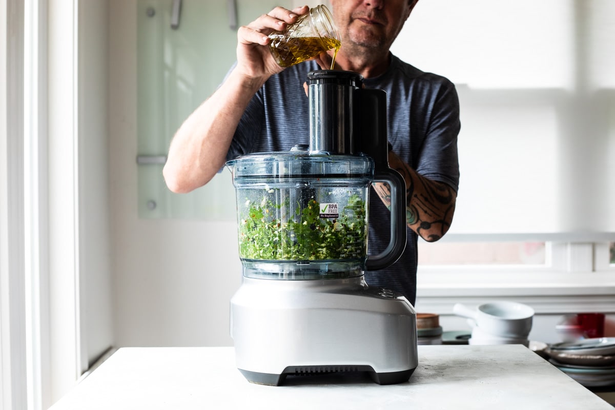 Oil being poured into a food processor to make chimichurri sauce.
