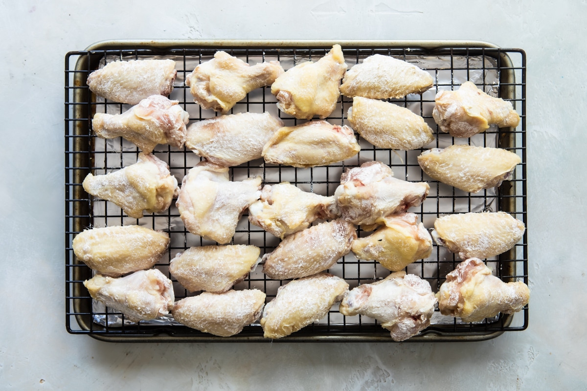 Raw wings on a baking rack over an aluminum foil lined baking sheet.