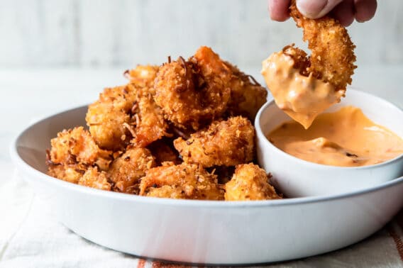 Someone dipping coconut shrimp in sauce.