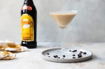 An espresso martini on a plate surrounded by espresso beans.