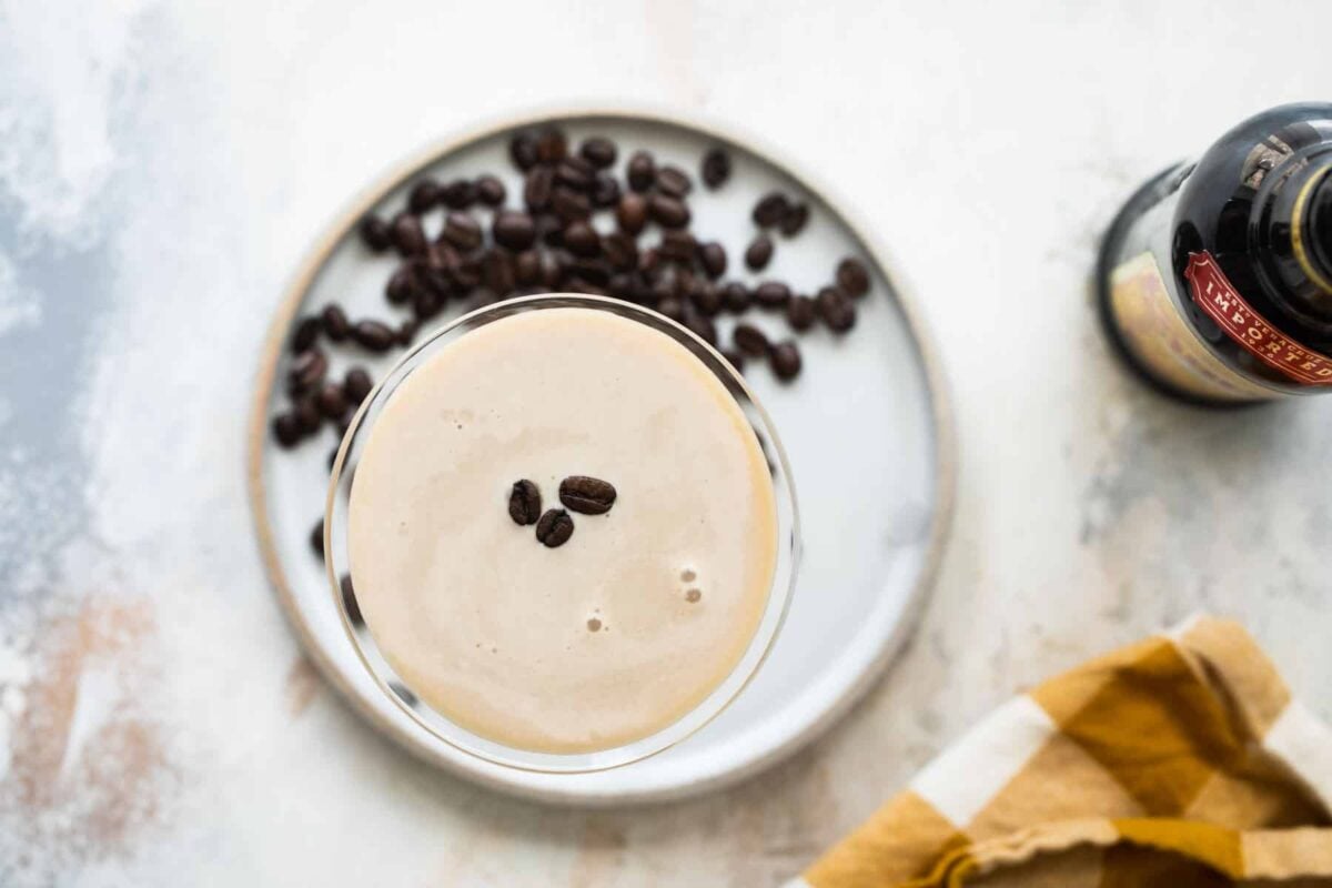 An espresso martini on a plate surrounded by espresso beans.