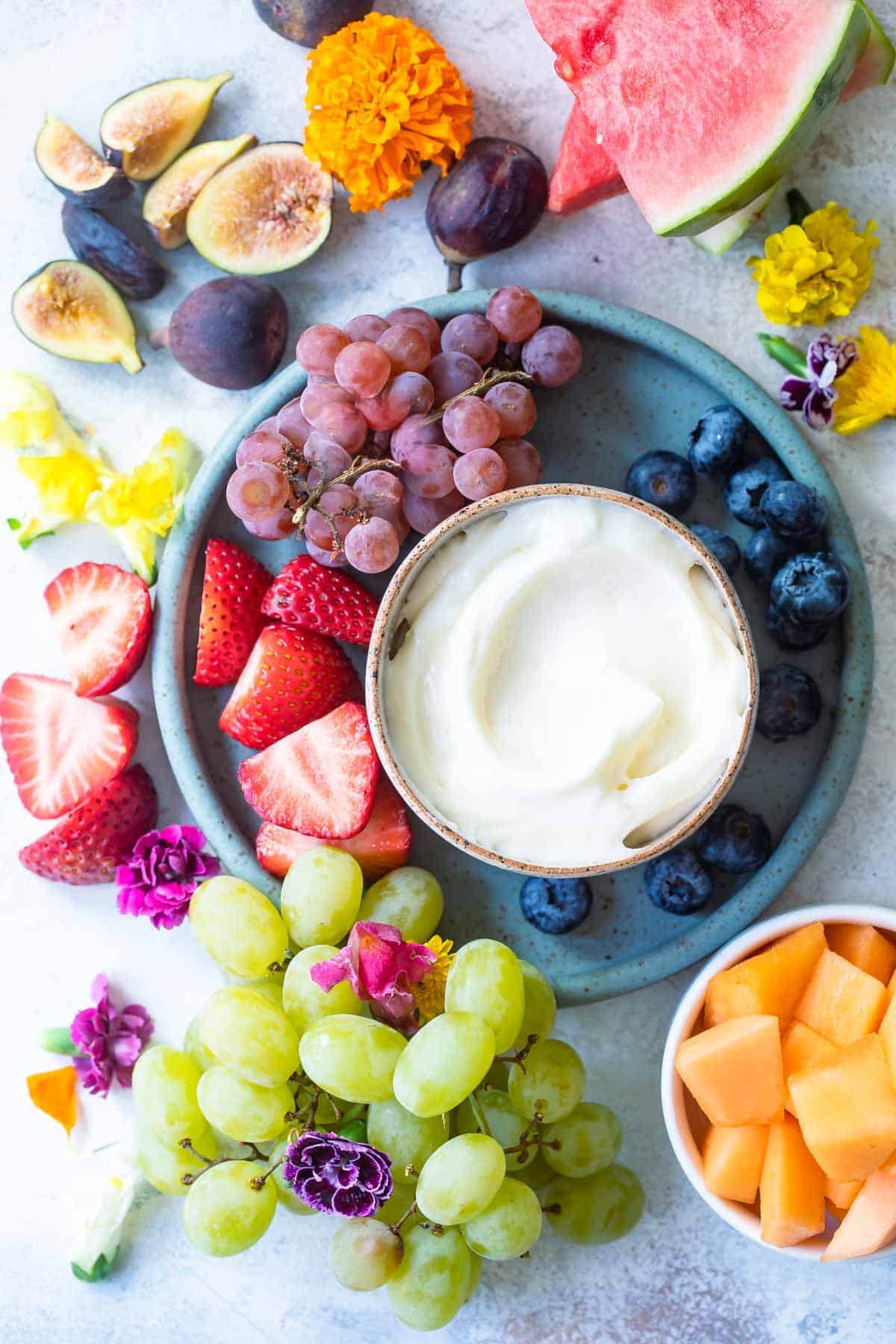 A bowl of fruit dip surrounded by fresh fruit.