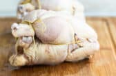 Two trussed Cornish hens on a wooden cutting board.