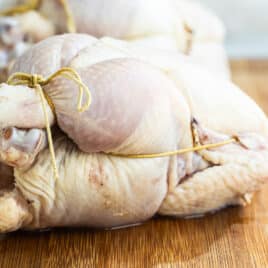 Two trussed Cornish hens on a wooden cutting board.