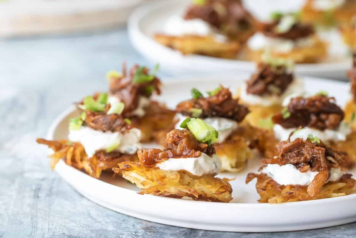 A platter of potato pancakes with bbq pulled pork and sour cream on top.