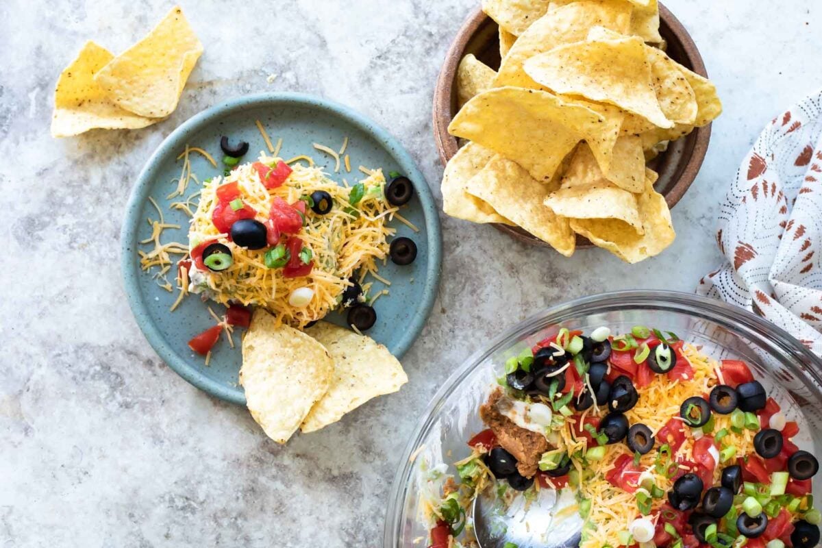 A pile of seven layer dip with chips.