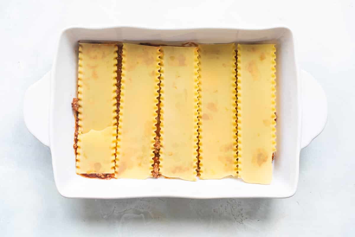 The best make ahead lasagna being assembled in a white baking dish.