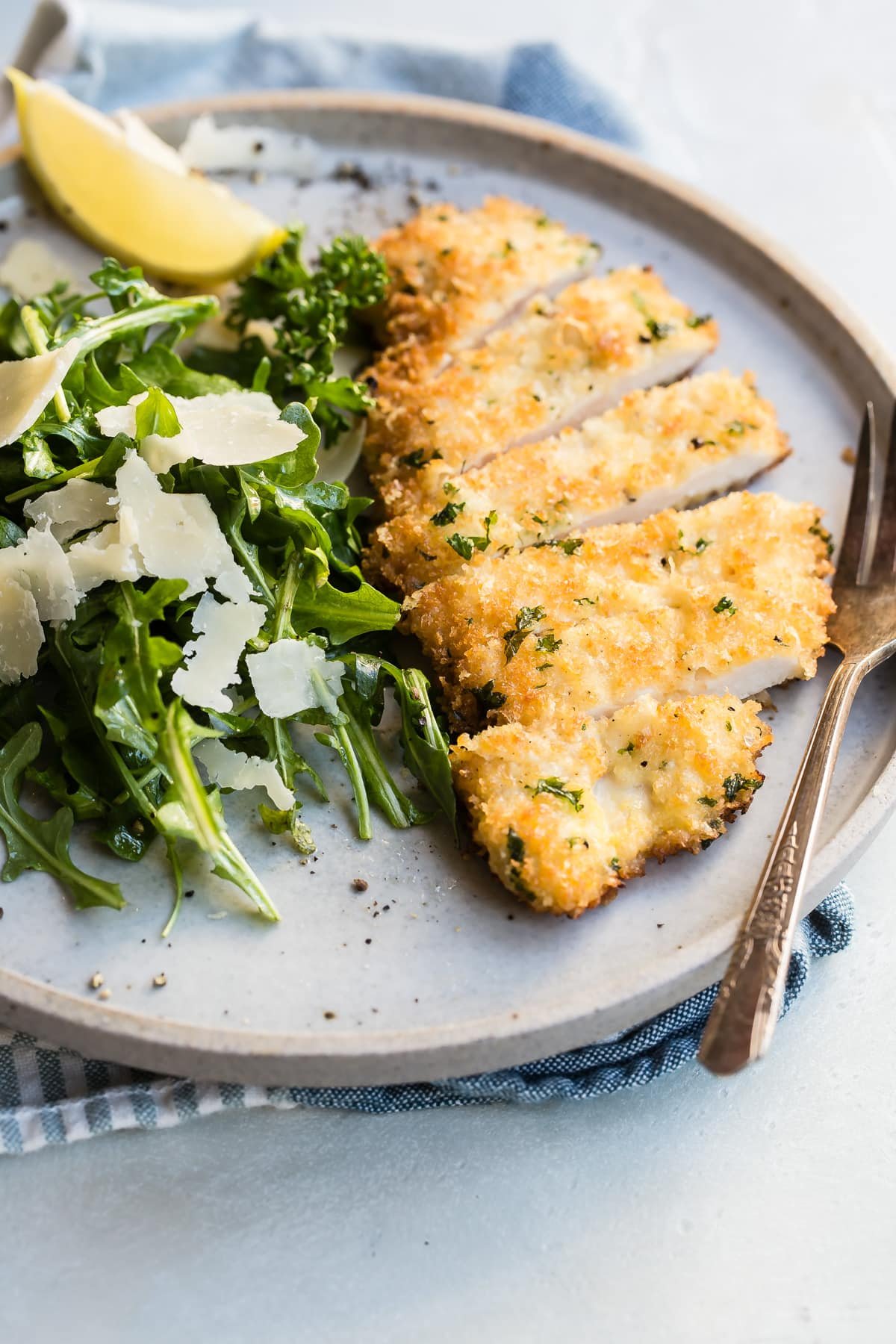 Chicken Milanese on a gray plate with a side of greens.
