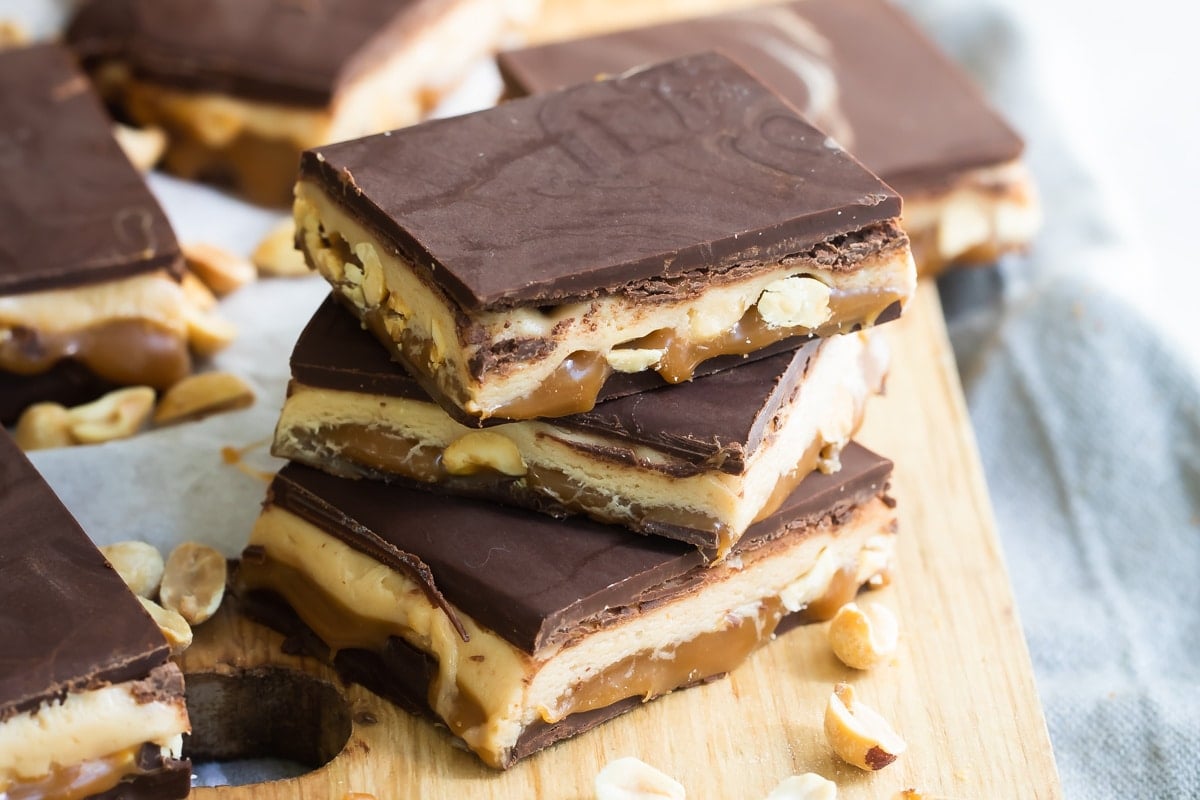 Homemade Snickers bars on a wooden cutting board.