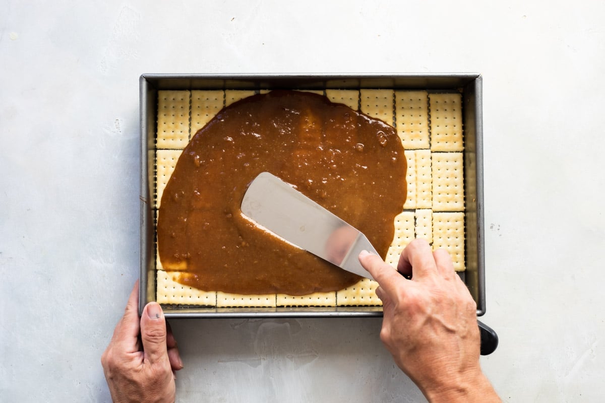 Layering crackers with caramel sauce for Twix bars.