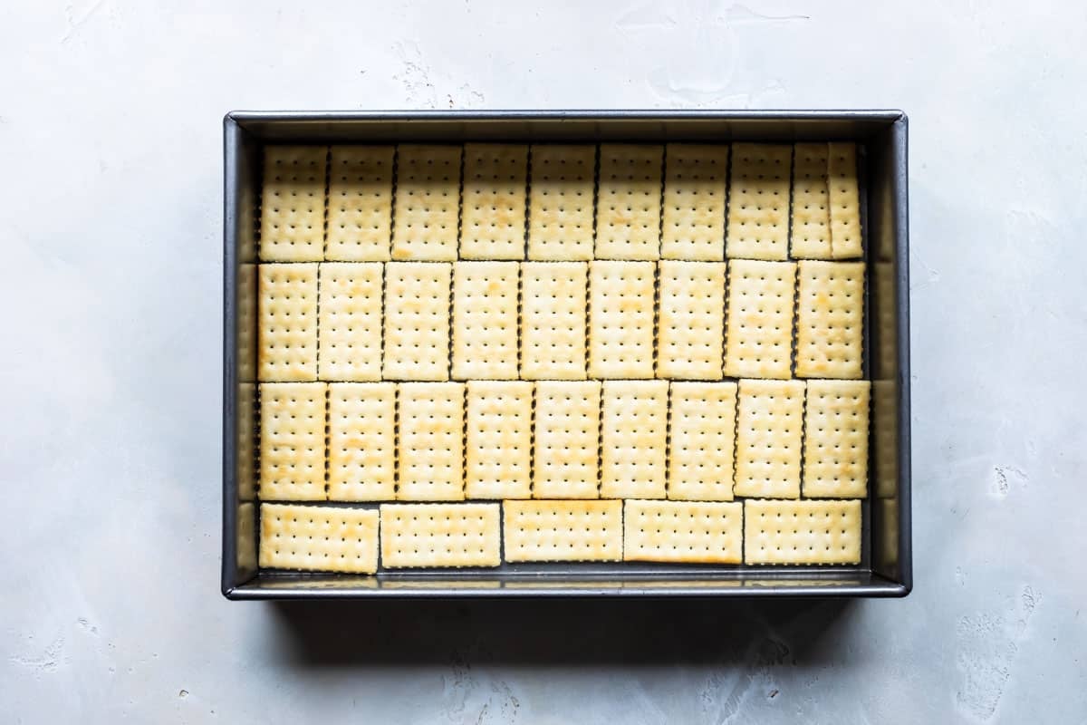 Layering crackers with caramel sauce for Twix bars.